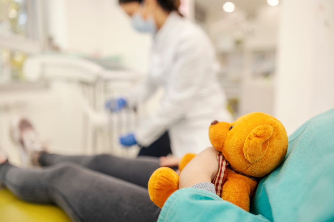 Cropped picture of a girl holding a teddy bear at dentist office.