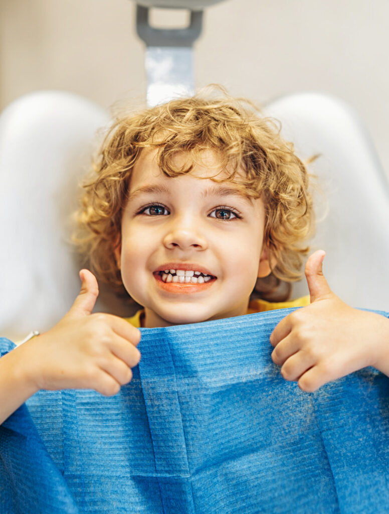 Happy cute little boy in dental ofiice showing thumbs up after treatment