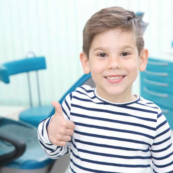 Cute little boy showing thumb up sign at dentist's office