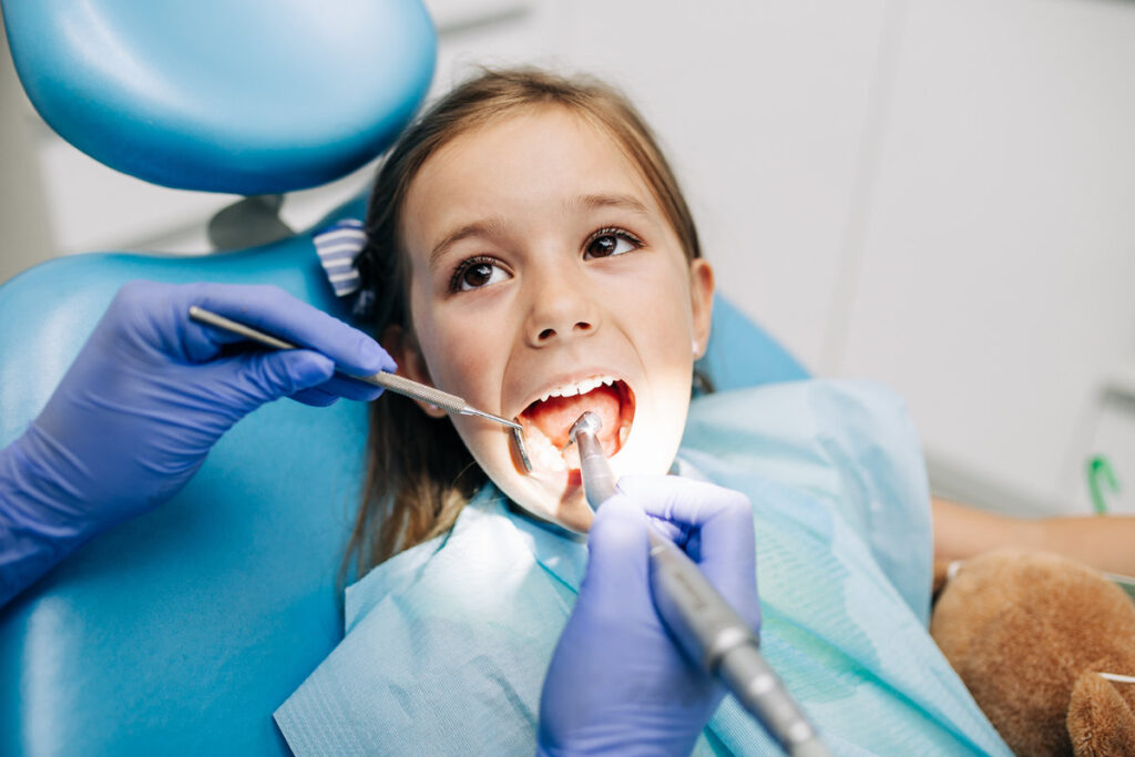 Cute little girl sitting on dental chair and having dental treatment.