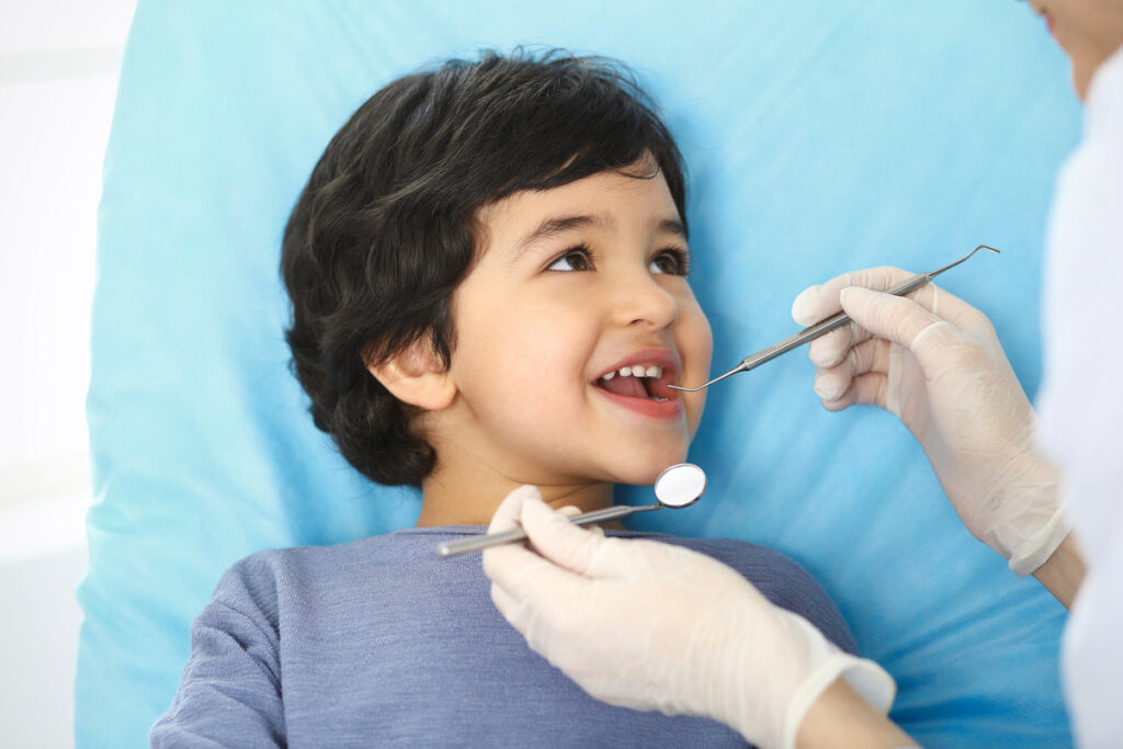 Little baby girl sitting at dental chair with open mouth during oral check up while doctor. Visiting dentist office. Medicine concept.