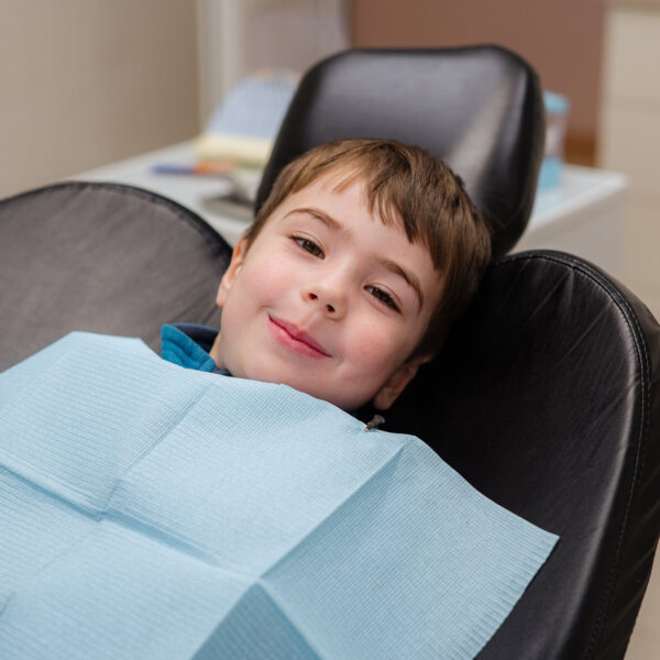 A cute little boy in a dental chair treats his teeth, smiling and happy