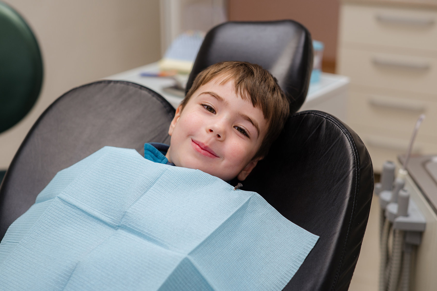A cute little boy in a dental chair treats his teeth, smiling and happy