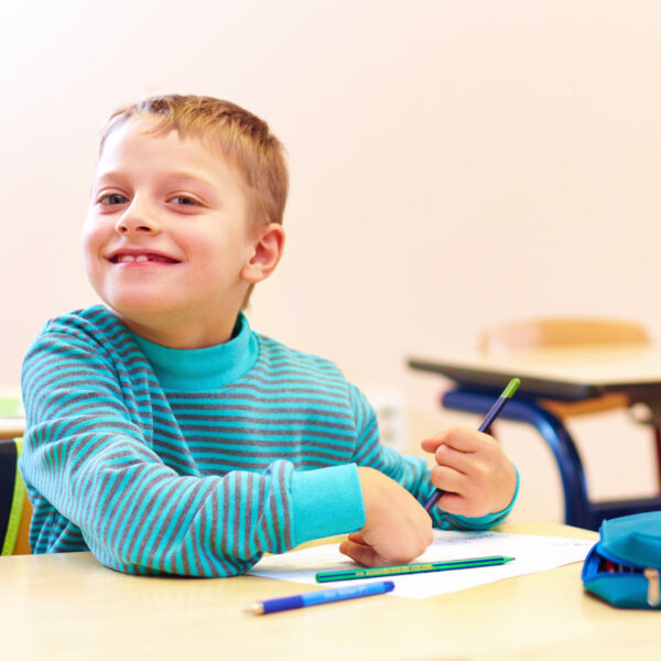 cute boy with special needs writing letters while sitting at the desk in class room