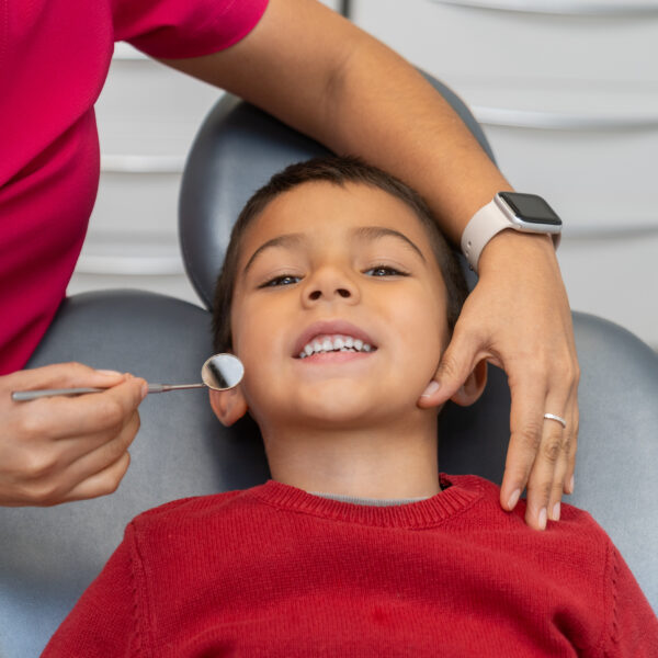 Pediatric dentist using a dental mirror to examine the teeth of a young boy during a routine checkup