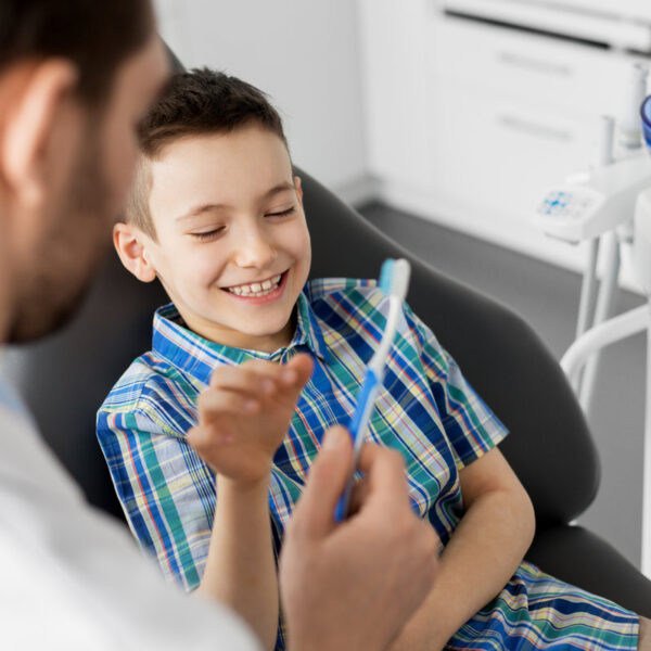 medicine, dentistry and healthcare concept - male dentist giving toothbrush to kid patient at dental clinic