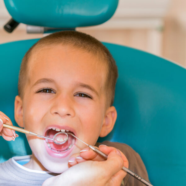 Pediatric dentist examining a little boys teeth in the dentists chair at the dental clinic. Dentist examining little boy's teeth in clinic.
