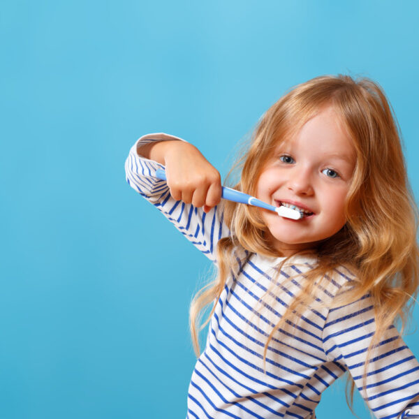 A little girl in striped pajamas is brushing her teeth with a toothbrush. The concept of daily hygiene. Isolated on a blue background