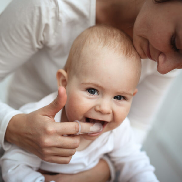 Mom helps to brush the teeth of a happy baby, Hygiene of the baby’s mouth, brushes her teeth with a special nozzle.