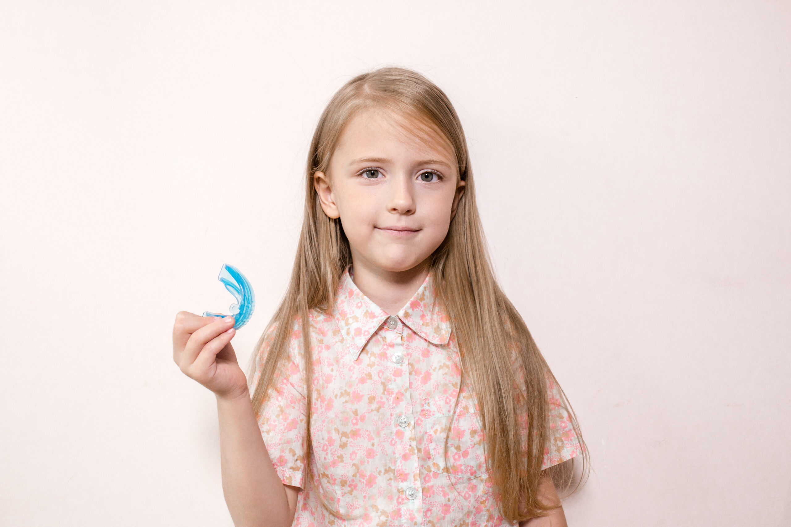 blond girl holds in hands silicone trainer for alignment of the teeth isolated on pink background