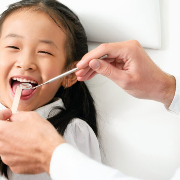 Friendly young dentist examining happy child teeth in dental clinic. Dentistry concept.