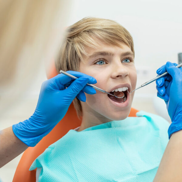 Blonde dentist examines the boy's teeth with a mouth mirror and dental probe