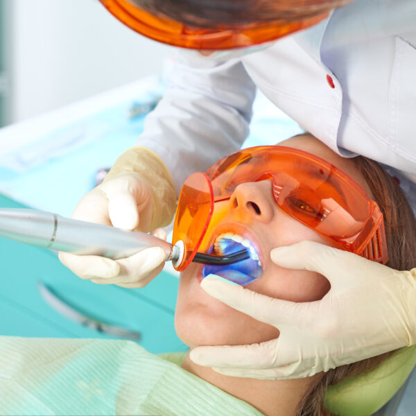 Girl child at the doctor. Dentist places a filling on a tooth with dental polymerization lamp in oral cavity. over clinic background.