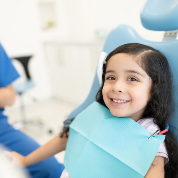 Smiling cute Hispanic girl sitting on chair at dental clinic