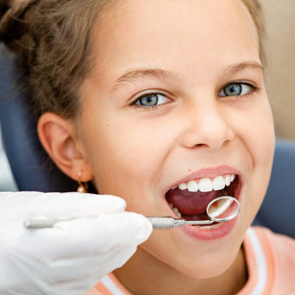 Little smiling girl, teeth check-up. Tooth exam using dental mirror close-up. Child's teeth treatment