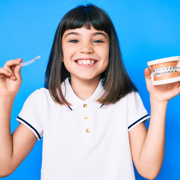 Young little girl with bang holding invisible aligner orthodontic and braces smiling with a happy and cool smile on face. showing teeth.