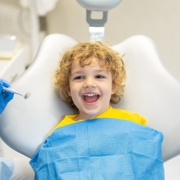 Cute young boy visiting dentist, having his teeth checked by female dentist in dental office
