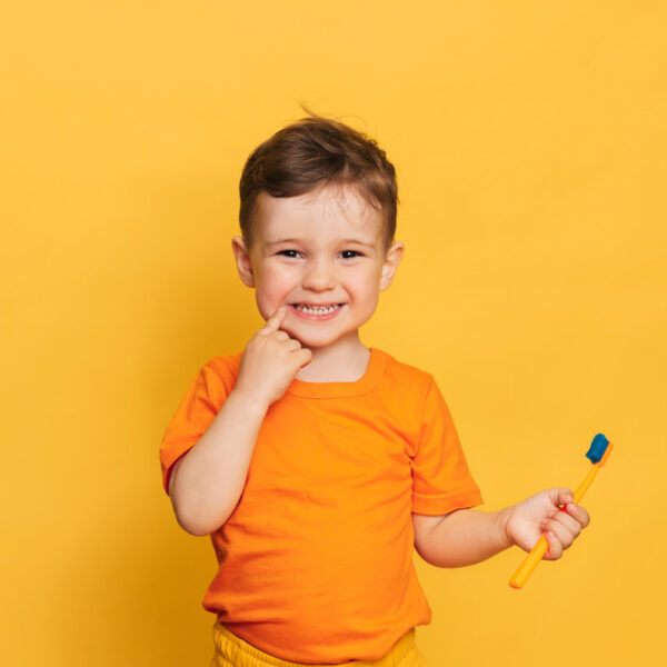 Happy baby toddler boy brushing his teeth with toothbrush on a yellow background. Health care, oral hygiene.