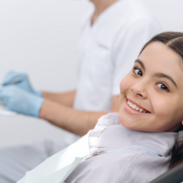 Attractive girl sitting in a dental chair, looking at the camera. Beautiful little girl smiling