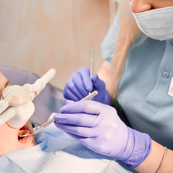 Female dentist checking child teeth with dental explorer and mirror while girl lying in dental chair with inhalation sedation at dental office. Concept of pediatric, sedation dentistry.