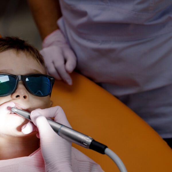 Close-up of a cheerful toddler with glasses in a dental chair. Five-year-old baby has his teeth examined and plaque is removed. Concept of dental care. High quality photo