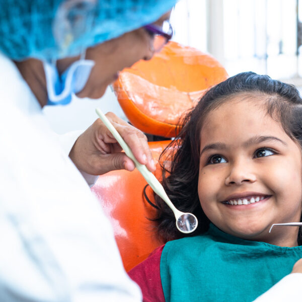 happy smiling kid looking at dentist while treating at hospital - concept of dental care, expertise and friendly hygienist
