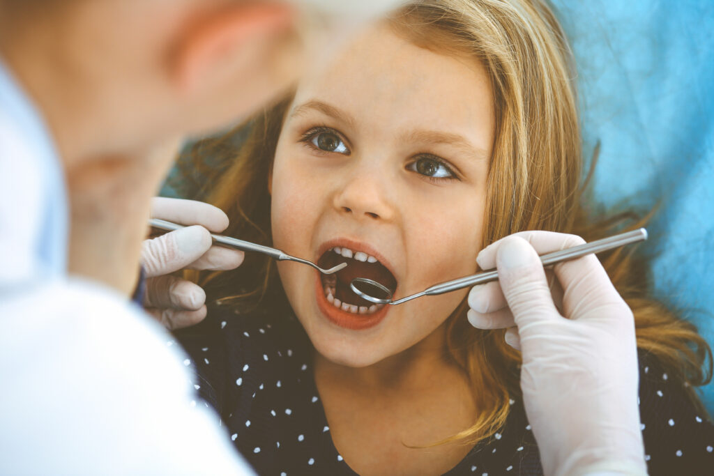 Little baby girl sitting at dental chair with open mouth during oral check up while doctor. Visiting dentist office. Medicine concept. Toned photo.