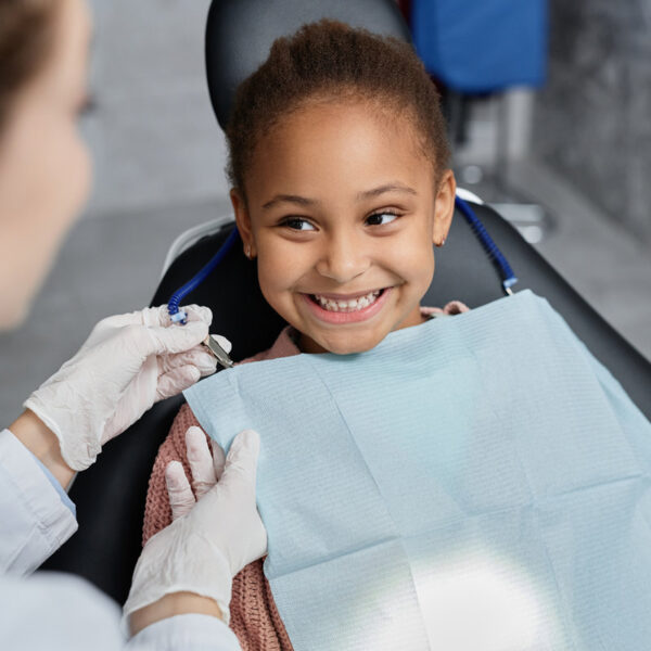 Portrait of smiling little girl in dental chair with nurse preparing her for teeth check up, copy space