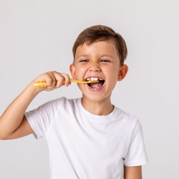 Morning concept. Close-up portrait of a happy laughing little boy with toothbrush on white background. A child in a white T-shirt brushes his teeth on his own. Space for text