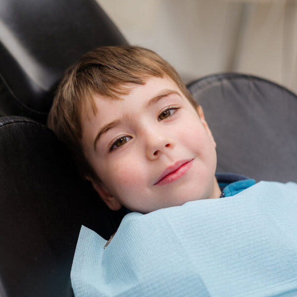 A cute little boy in a dental chair treats his teeth, smiling and happy
