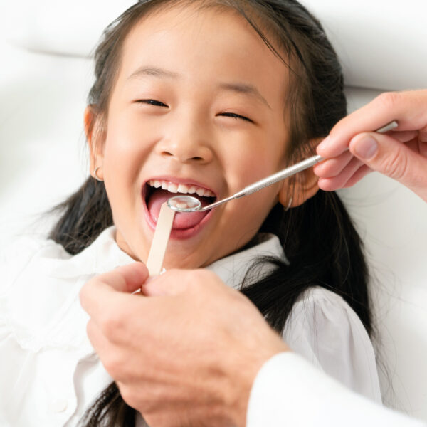 Friendly young dentist examining happy child teeth in dental clinic. Dentistry concept.