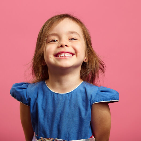 Female portrait of charming child of three years with a beautiful smile, cheerful shot on isolated pink.