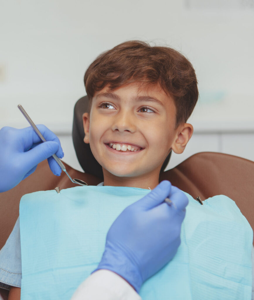 Adorable happy healthy boy smiling cheerfully at his dentist, sitting in a dental chair. Cropped shot of a professional dentist checking teeth of a lovely boy