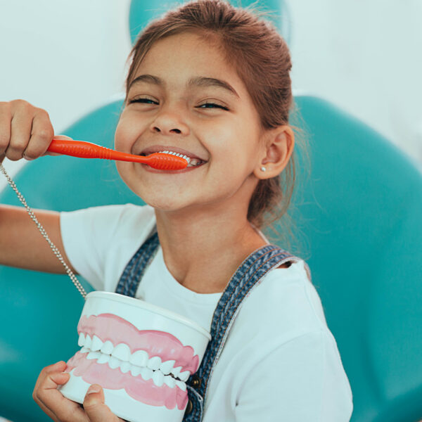 smiling mixed raced girl brushing teeth at dental clinic