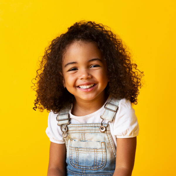 Happy african-american child girl smiling to camera over yellow background
