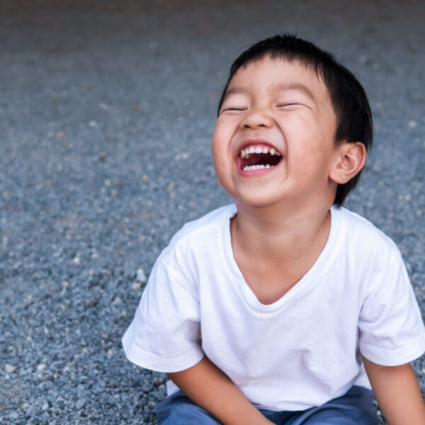 Asian cute little child boy laughing with mouth open wide, seeing whitening teeth. Happy Kid in white shirt enjoy in funny shot in relaxing day.