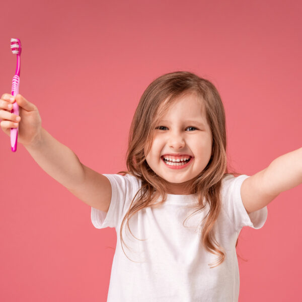 happy little 4-year-old girl, smiling with healthy white teeth and showing a gesture of approval, class on a pink background. Oral hygiene. Daily brushing of teeth, 2 times a day.