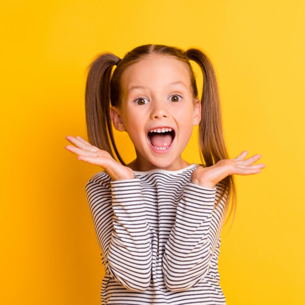 Portrait of young excited shocked crazy smiling girl child kid hold hands isolated on yellow color background.