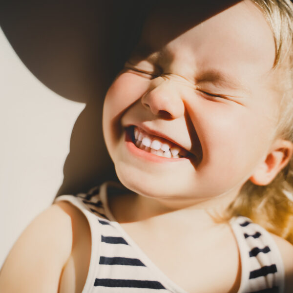 Cutest little girl smiling and squinting in sunlight. Happy toddler having fun. Portrait of playful child preschool age. Lifestyle photography.