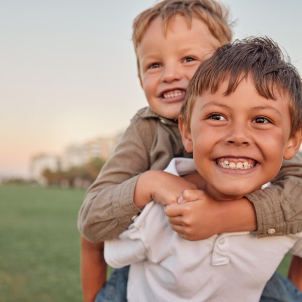 Happy, smile and portrait of brothers with piggyback ride playing in a park together on vacation. Happiness, excited and children bonding in nature while on a summer holiday adventure in Australia