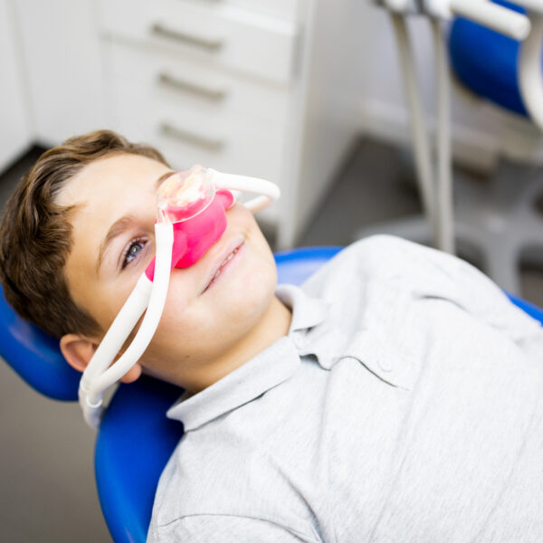 Fear of the dentist! A little boy sits in a dentist's office wearing a nasal mask to breathe nitrous oxide to relax. Concept of feeling relaxed with laughing gas.
