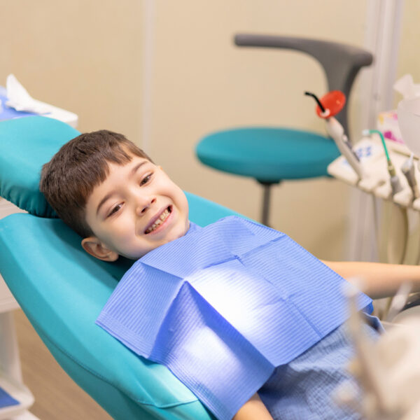 kid in dental office. dentist checking child teeth using tools mouth mirror and scalar.crying with tears, sad boy is afraid.doctor looking at screen,tooth filling treatment.kid in chair being examined