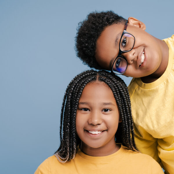 Smiling African American kids bonding together looking at camera isolated on blue background. Childhood and friendship concept