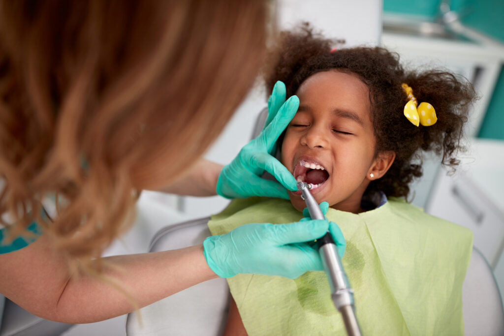 Nice female dentist patiently polish teeth to child in dental practice